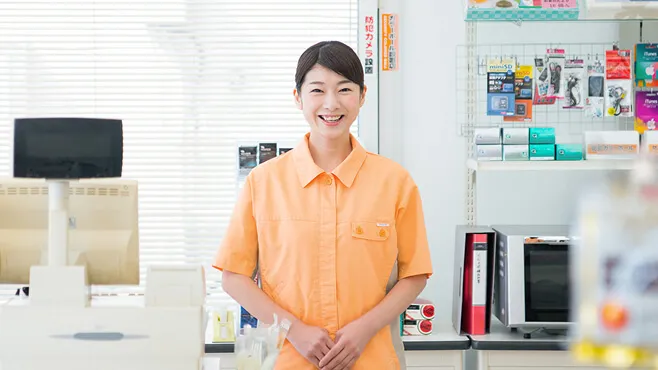コンビニのレジ前で笑顔で立つオレンジの制服を着た女性スタッフ。