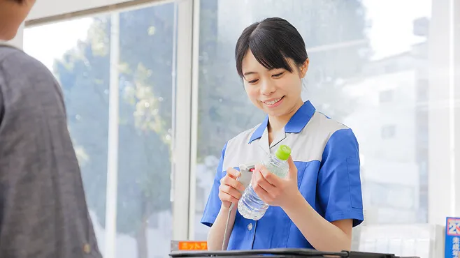 ペットボトルを持ち、レジで対応する青い制服の女性スタッフ。